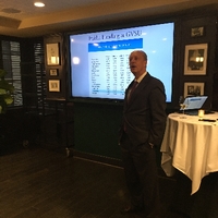 older male alumni addressing the room with a powerpoint behind him
